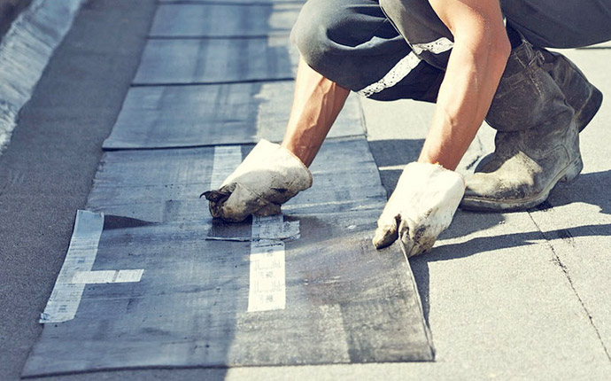 Gloved hands positioning flat-roof membrane material
