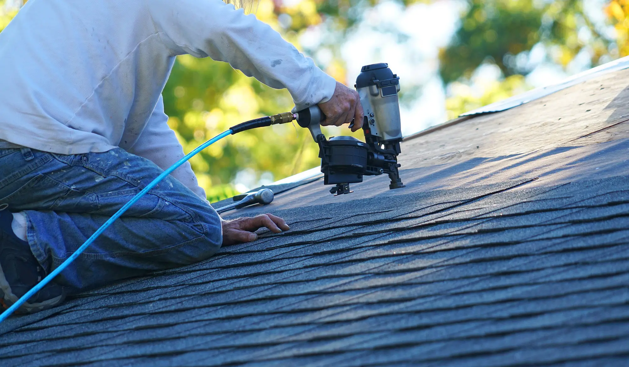 Illustrative roofer using a nail gun on shingles