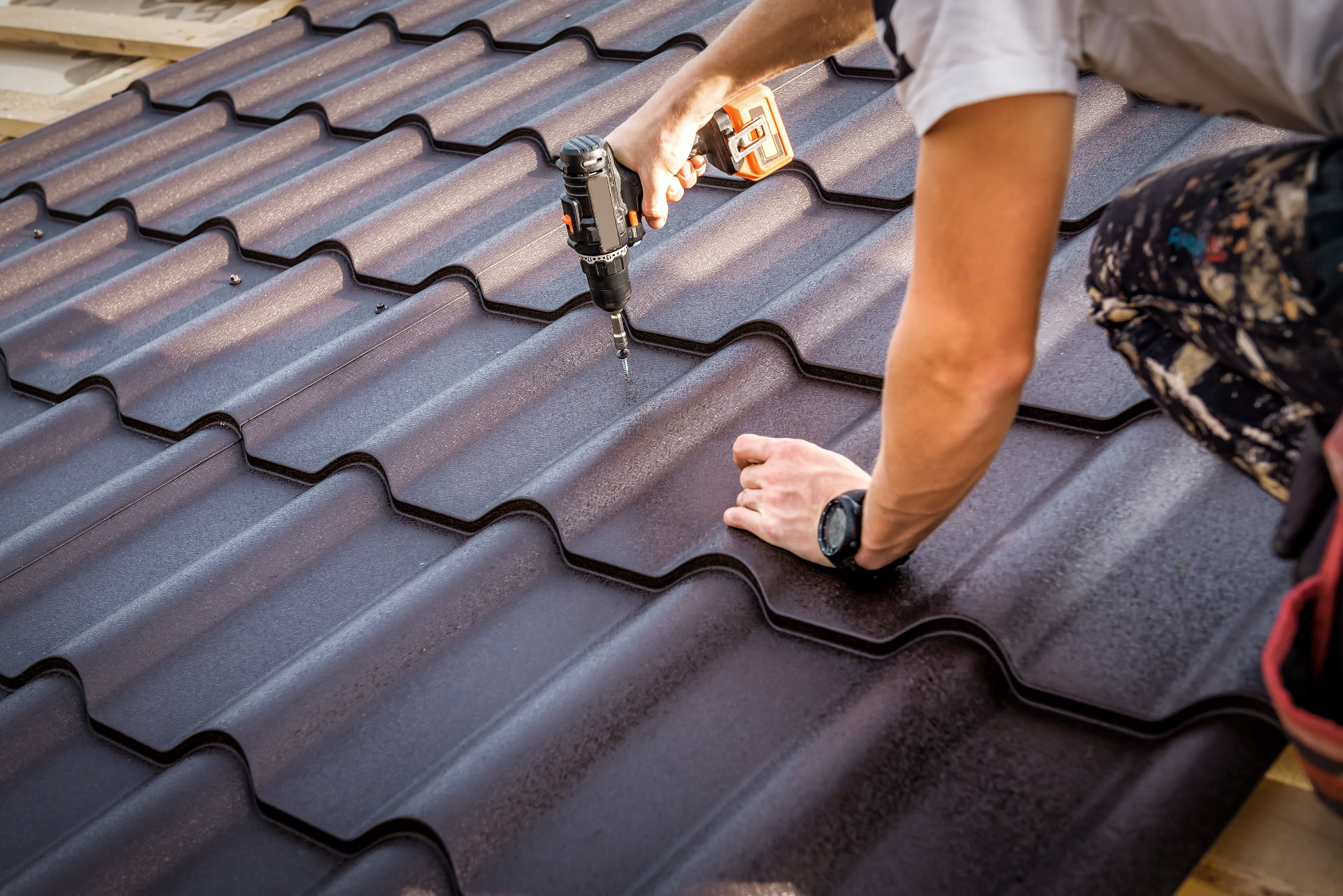 Illustrative worker fastening metal tile roofing with a drill
