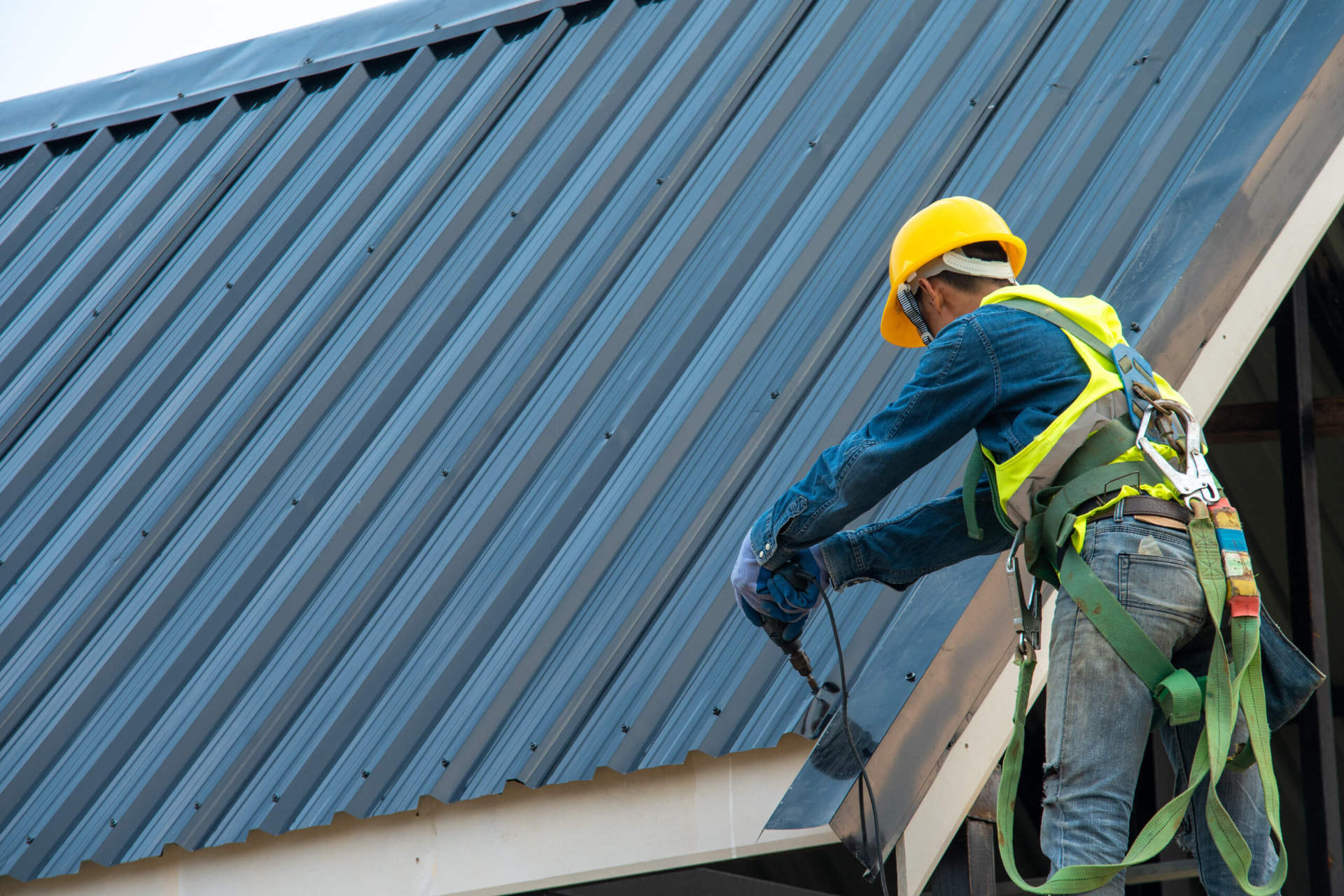 Worker fastening metal roofing with a drill
